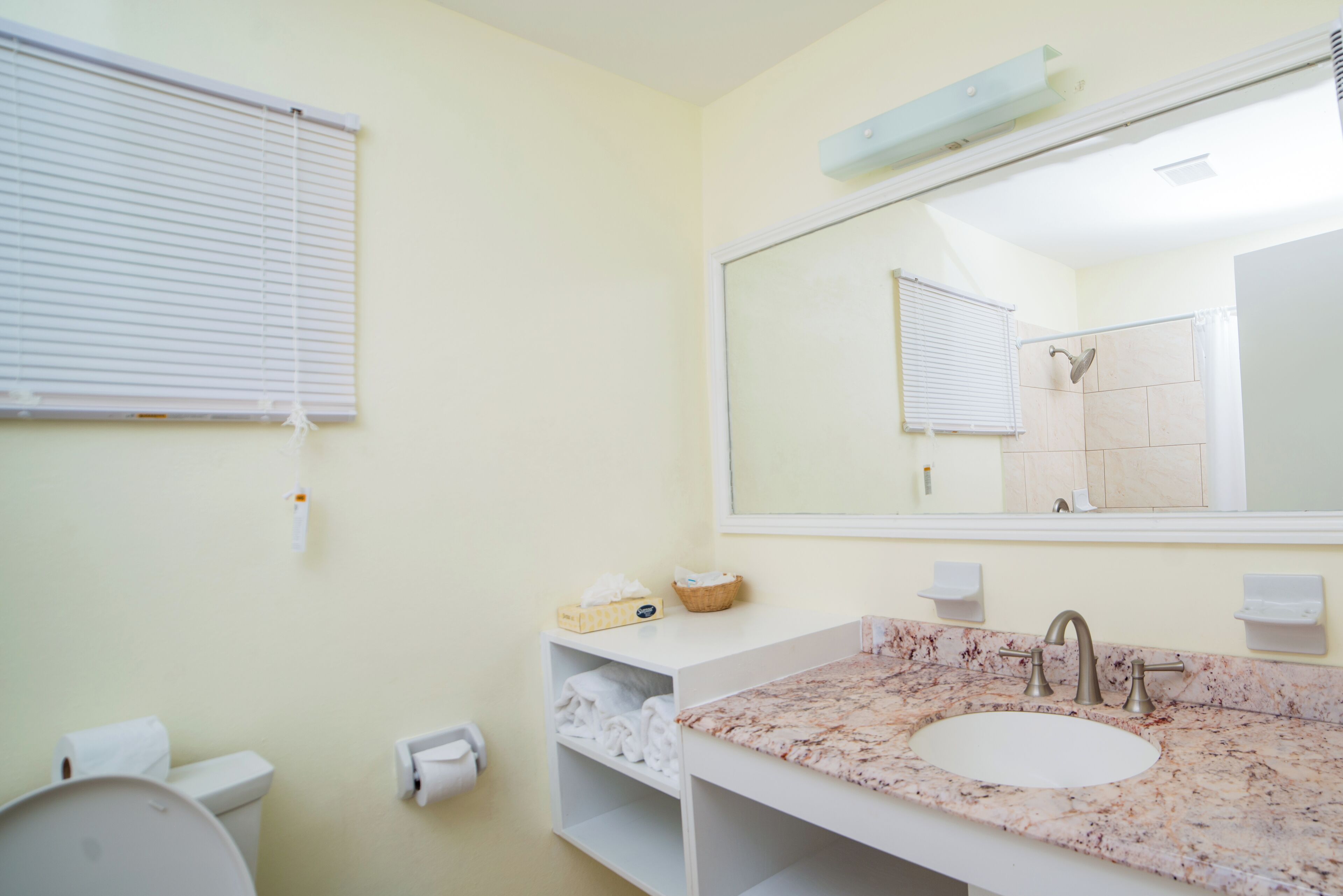 Un baño con lavamanos blanco, un espejo grande, inodoro y estante con toallas.