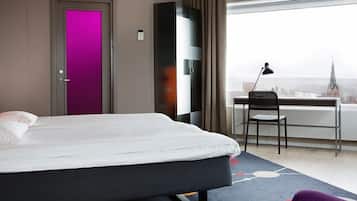 A hotel room with a bed, a desk with a chair, and a view of a cityscape.
