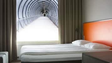 Ein Hotelzimmer mit Bett, Nachttisch, einem Fenster mit Vorhängen und Blick auf einen Tunnel.