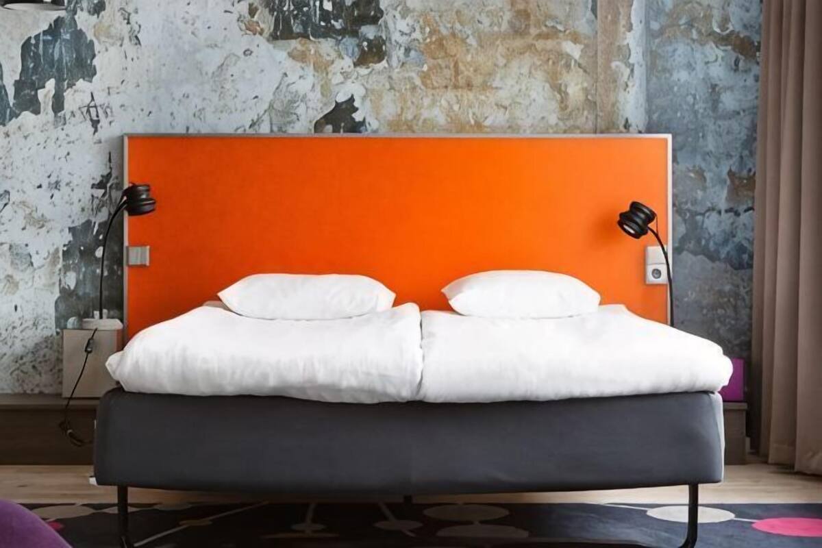 A bed with an orange headboard, white bedding, and a black mattress.