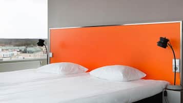 A bed with white bedding and two white pillows, a nightstand with a lamp, and a window with a view of buildings.