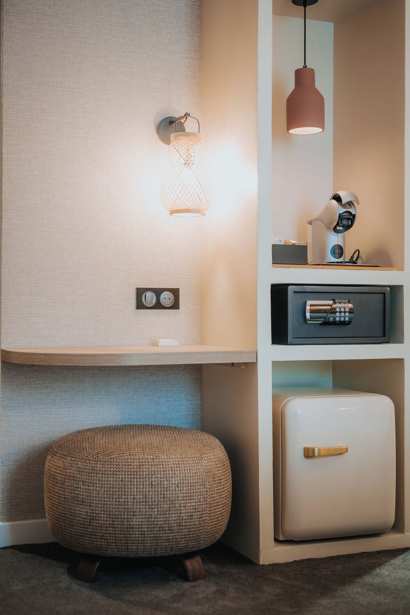 A modern room with a textured wall, a round woven ottoman, a white cabinet, a pink pendant light, and a security device on the wall.