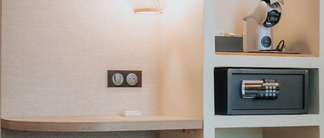 A modern room with a textured wall, a round woven ottoman, a white cabinet, a pink pendant light, and a security device on the wall.