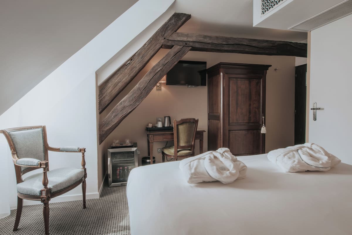 A bedroom with a large bed, two chairs, a wooden cabinet, and a fireplace.
