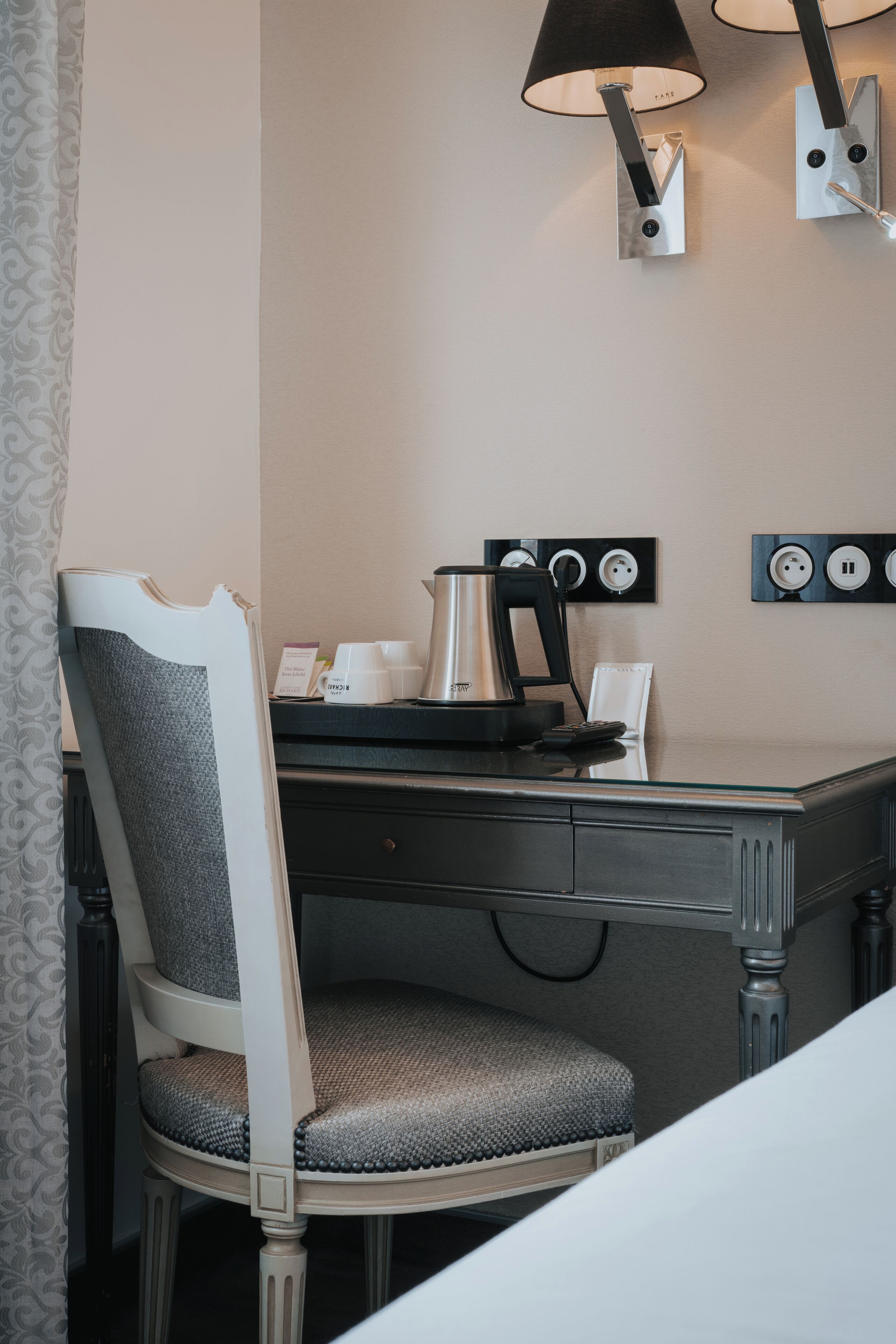 Una camera d'albergo con una scrivania, una sedia, una macchina del caffè e lampade a parete.