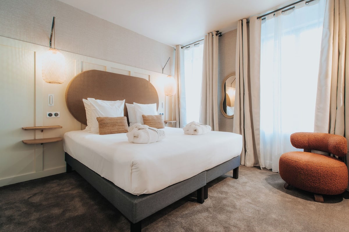 A hotel room with a large bed, a bedside table, a mirror, and a seating area with a chair.