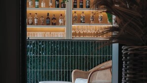 A bar area with shelves of liquor bottles and glasses, a seating area with two white tables and chairs, and a green tiled wall.
