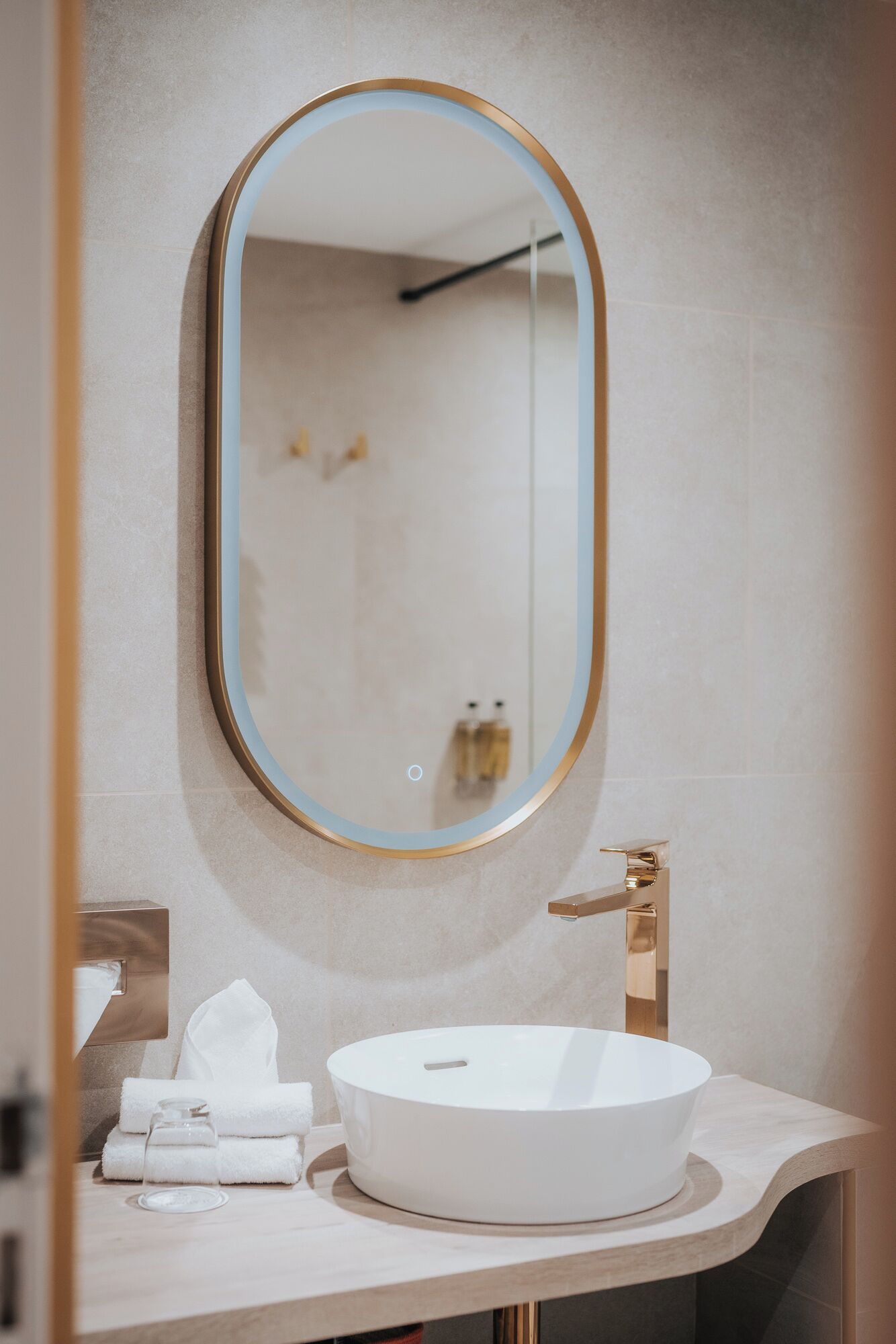 A bathroom with a round white sink, a gold faucet, and a mirror with a gold frame.