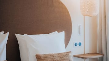 Cama bem arrumada com almofadas brancas e castanhas, luminária pendente e pequena mesa de cabeceira de madeira.