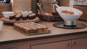 A breakfast buffet with various food items, including jars of spreads, a bowl of fruit, and baskets of bread.