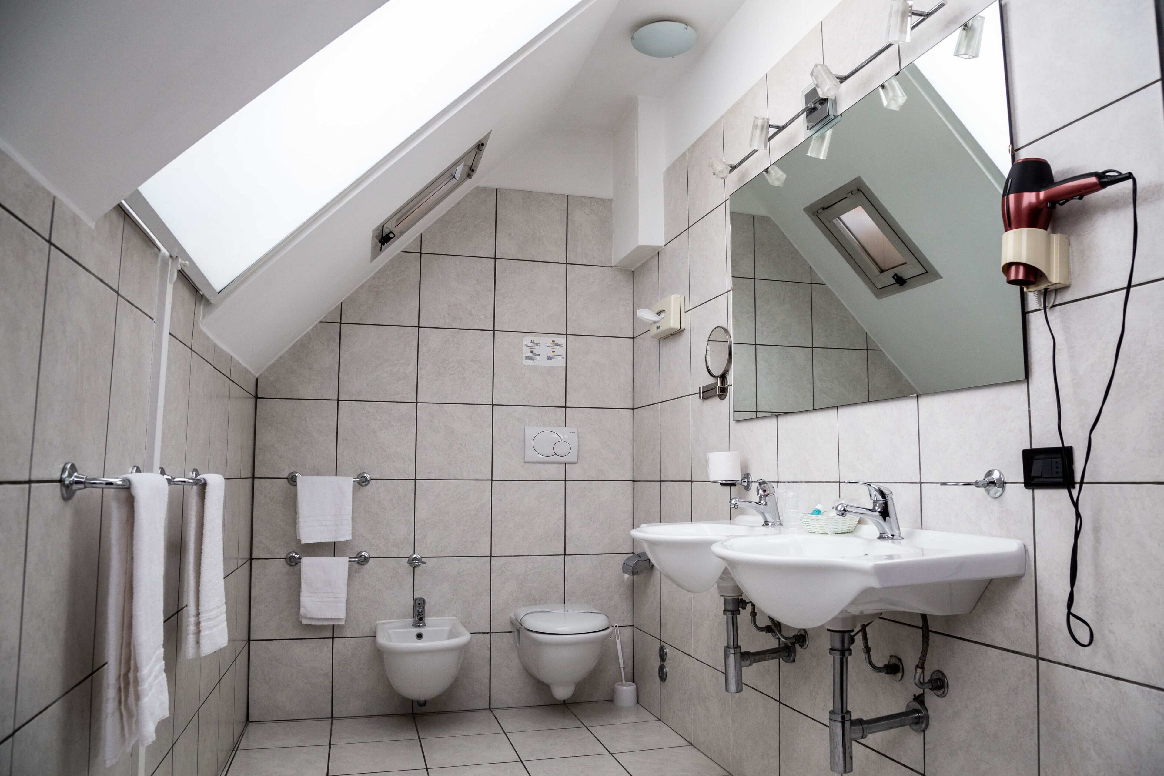 A modern bathroom with two sinks, a bidet, and a skylight.