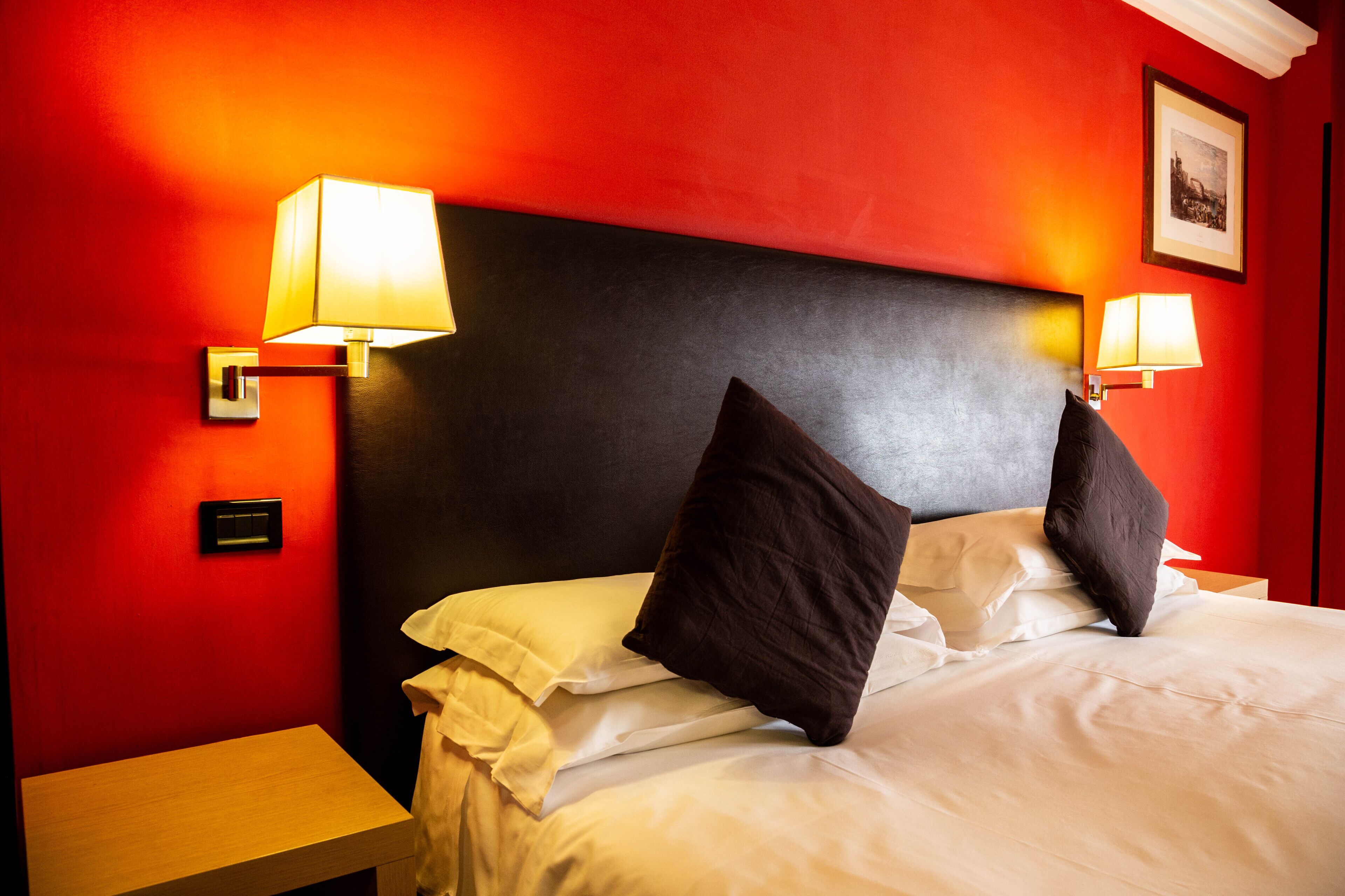 A hotel room with a red wall, a black headboard, and two bedside lamps.