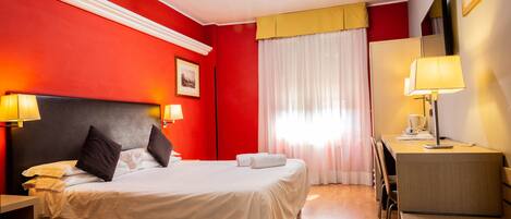 A hotel room with a bed, bedside tables, a desk, and a chair.