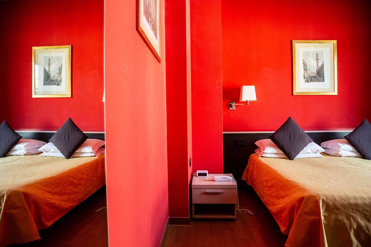 A mirrored room with two beds, red walls, and framed pictures.