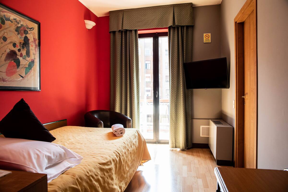 A hotel room with a bed, a chair, a TV, and a window with curtains.