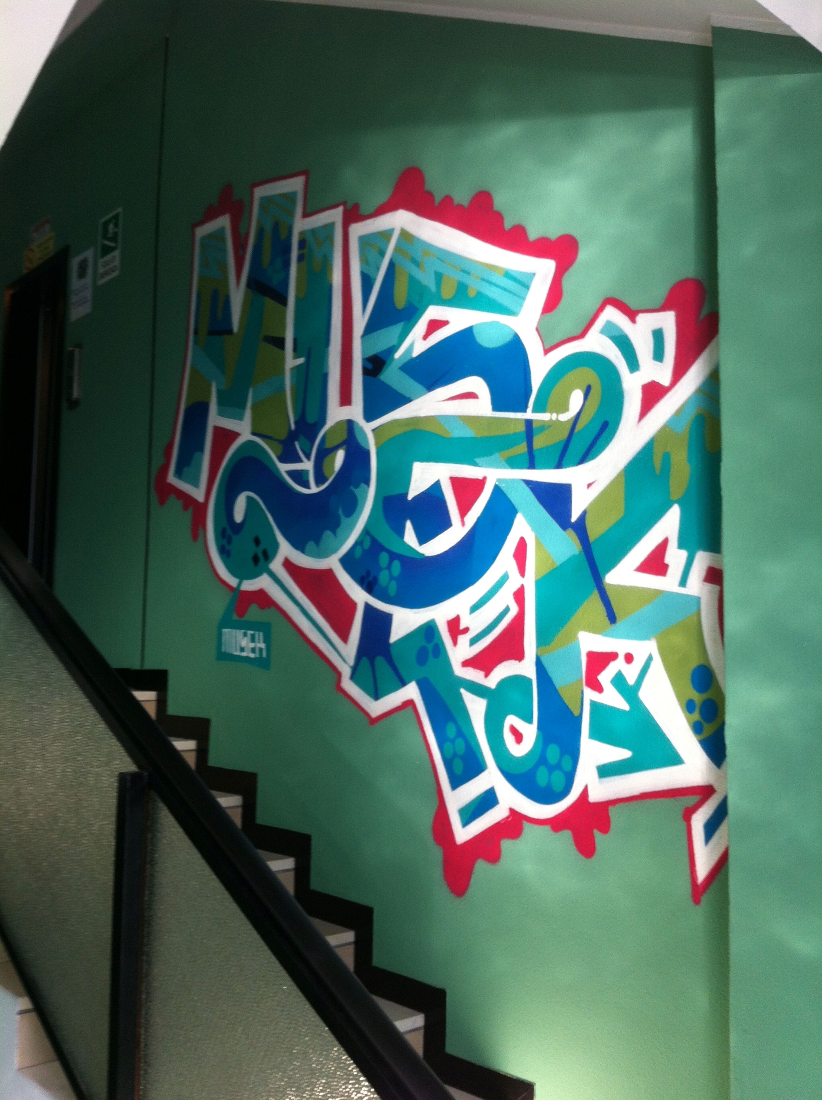 Una escalera con un muro verde decorado con grafitis coloridos.