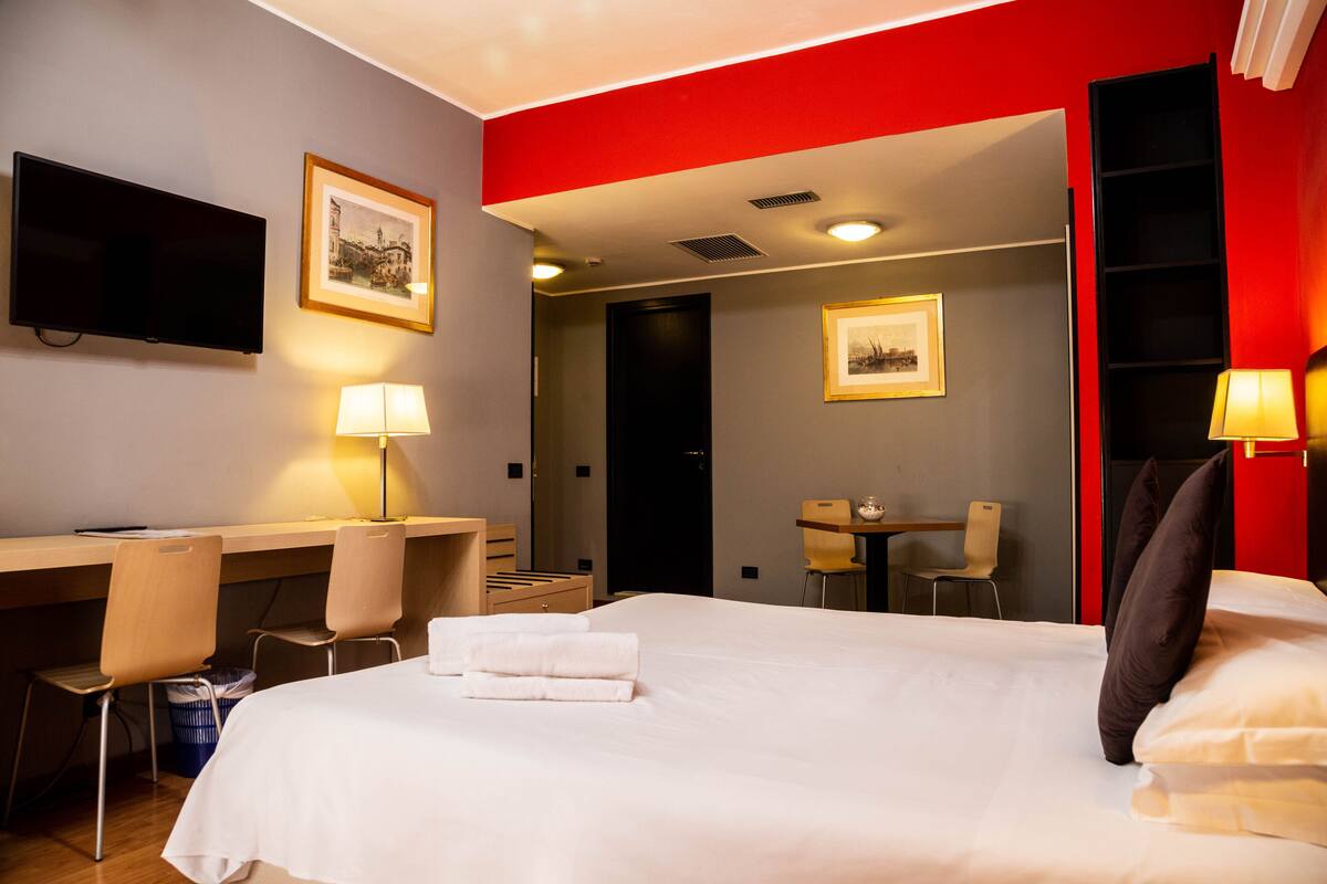 A hotel room with a bed, desk, chairs, and a TV.
