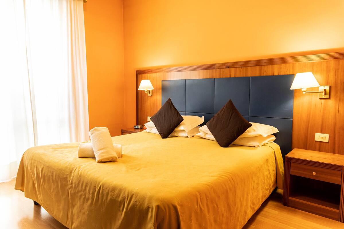 A hotel room with a large bed, two bedside tables, and a headboard with wall-mounted lamps.