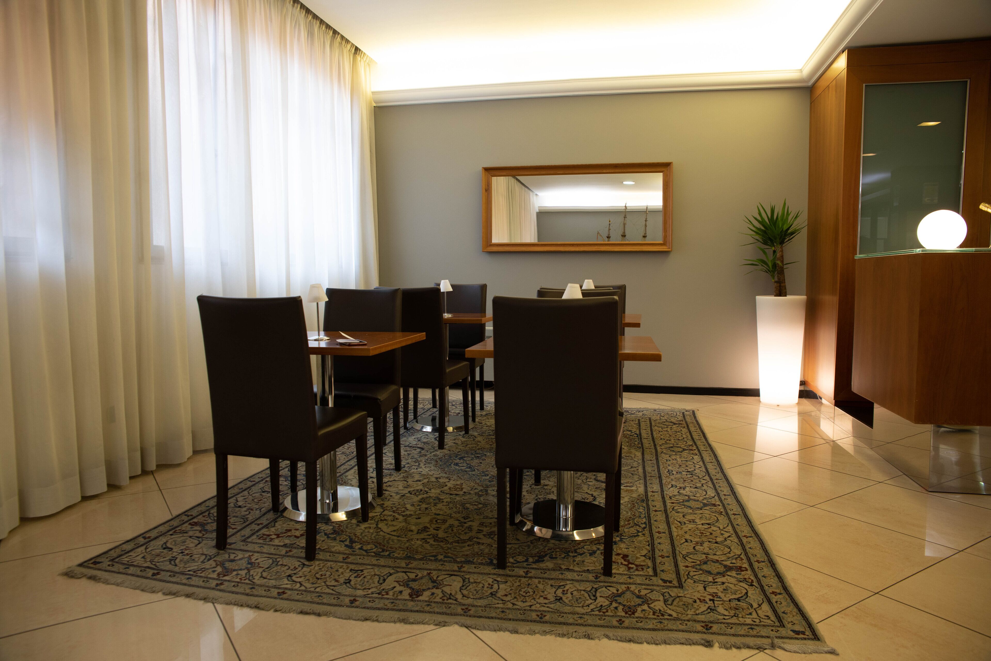 A hotel room with a dining area featuring a table and chairs, a large mirror, a potted plant, and a modern cabinet.
