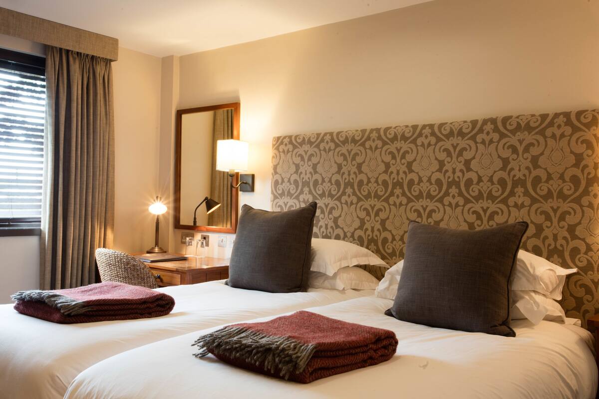 Une chambre d’hôtel avec un grand lit, deux oreillers, une table de chevet avec une lampe et une fenêtre avec des rideaux.
