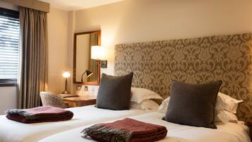 A hotel room with a large bed, two pillows, a bedside table with a lamp, and a window with curtains.