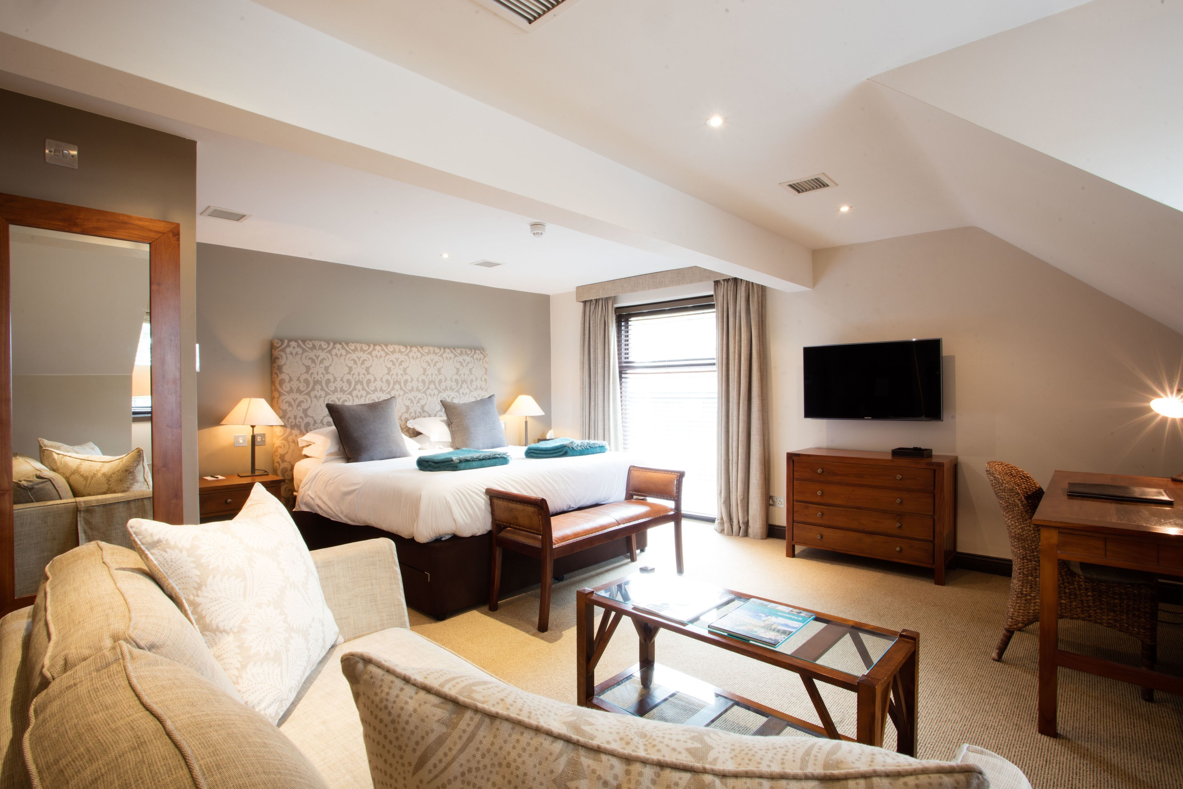A hotel room with a bed, a sofa, a desk, a TV, and a window.