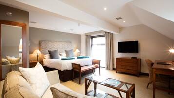 A hotel room with a bed, a sofa, a desk, a TV, and a window.