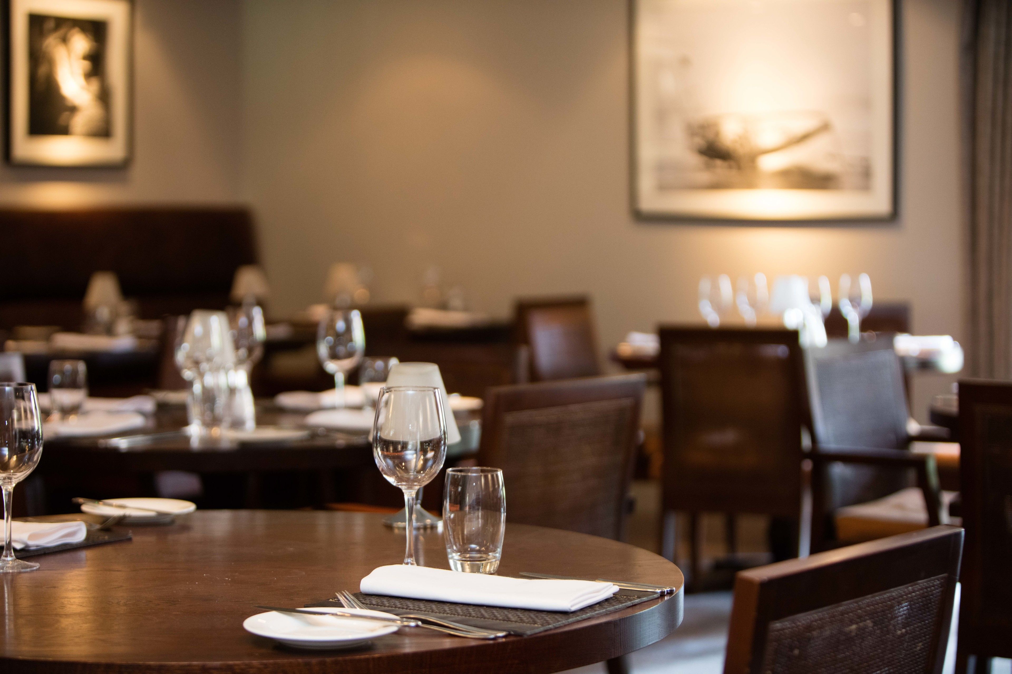 Un interior de restaurante con mesas dispuestas para comer, sillas y cuadros en las paredes.