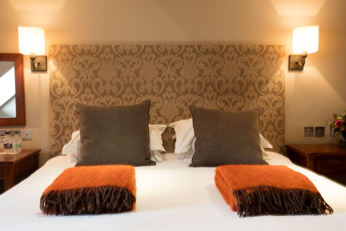 Une chambre d’hôtel avec un grand lit, deux oreillers, une tête de lit à motifs et deux lampes fixées au mur.