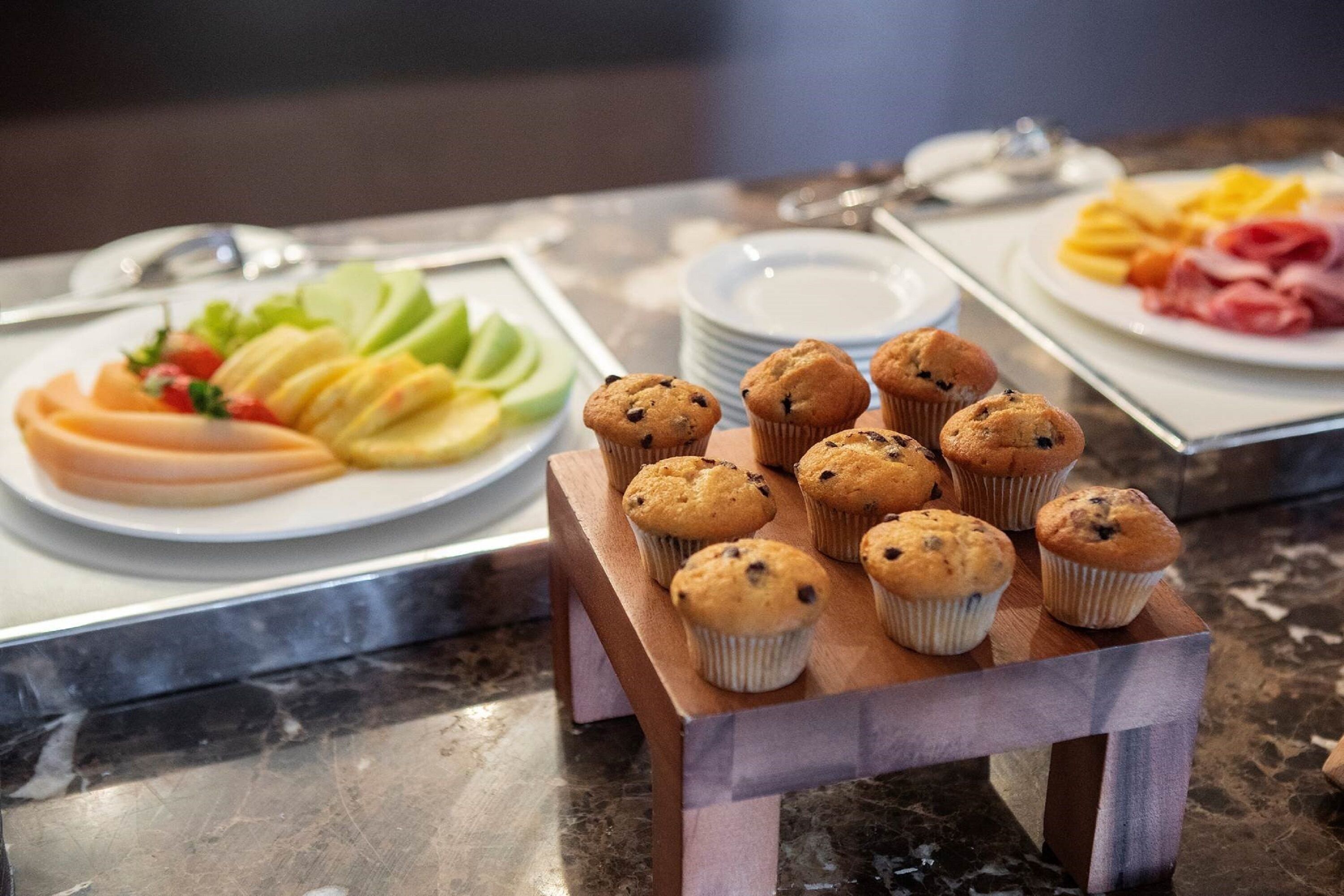 A buffet table with various food items including muffins, sliced fruits, and a selection of meats.