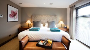 A hotel room with a large bed, two bedside tables with lamps, a tray with breakfast items, and a window with curtains. - Barnham Broom Hotel, Golf & Spa (Norwich)