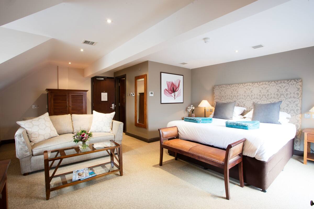 Une chambre d’hôtel comprenant un lit, un canapé, une banquette, une table basse et un tableau accroché au mur.