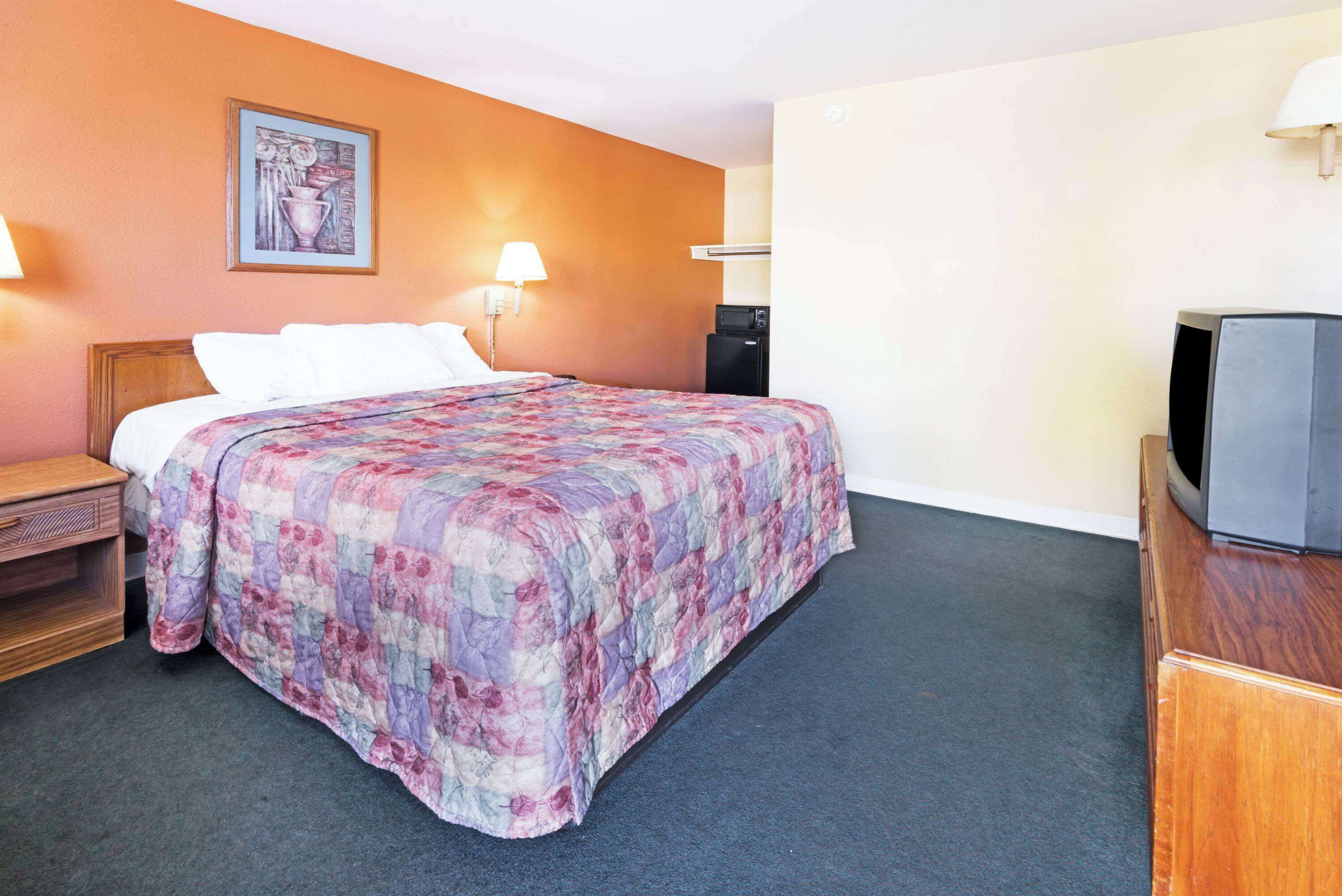A hotel room with a bed, a TV, a desk, and a lamp.