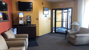 Un vestíbulo de hotel con una recepción, un televisor, una máquina de café y una zona de estar.