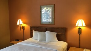 Una habitación de hotel con una cama, dos lámparas de noche, una mesita de noche con un teléfono y un cuadro en la pared.