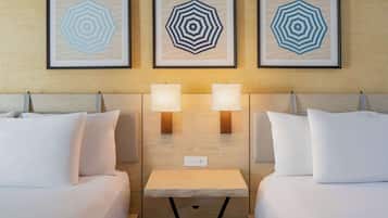 A hotel room with two beds, a small table, and three framed artworks on the wall.