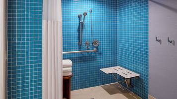 A bathroom with blue-tiled walls, a shower with a handheld showerhead, a towel rack, and a small stool.