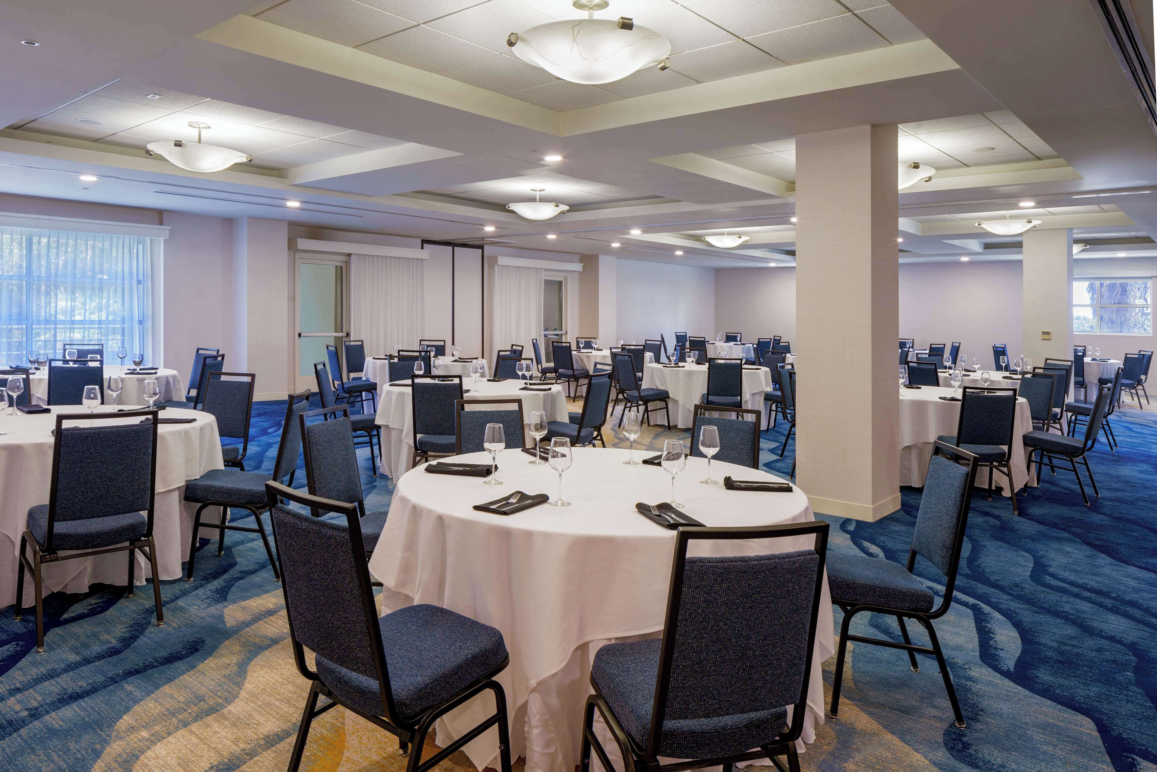 A conference room with multiple round tables, each set with chairs, glasses, and cutlery.