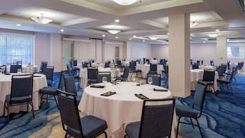 Un salón de conferencias con varias mesas redondas, cada una con sillas, vasos y cubiertos.