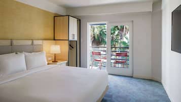 A hotel room with a large bed, a nightstand with a lamp, a wardrobe, and a balcony with red chairs.