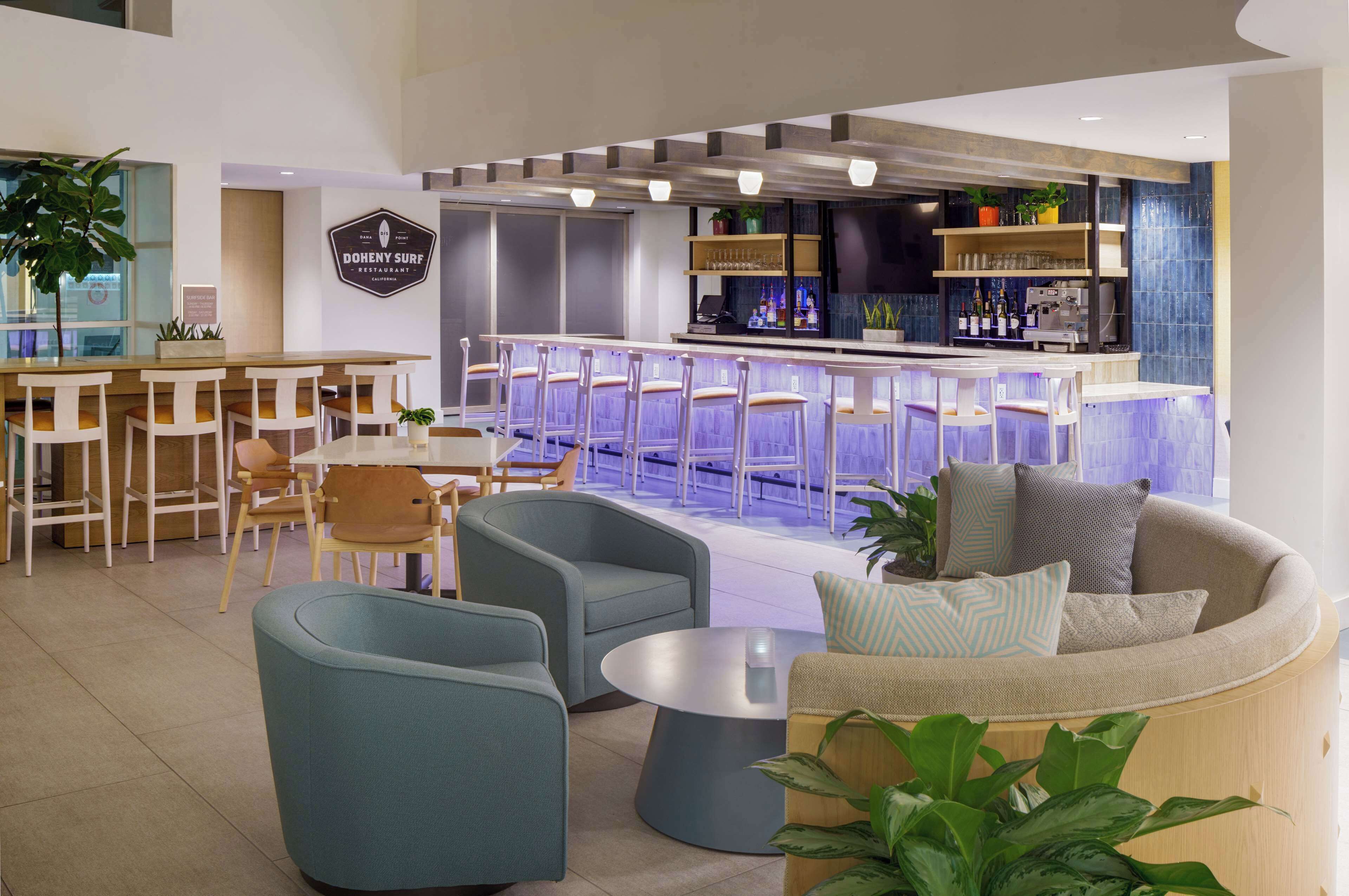 A modern bar area with a bar counter, seating, and a sign for 'Doheny Surf Restaurant'.