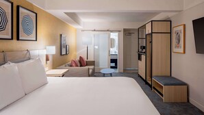 A hotel room with a large bed, a sofa, a small round table, and a bench. There is a wardrobe, a mirror, and a door leading to a bathroom. - Hilton Garden Inn Dana Point Doheny Beach (Dana Point)