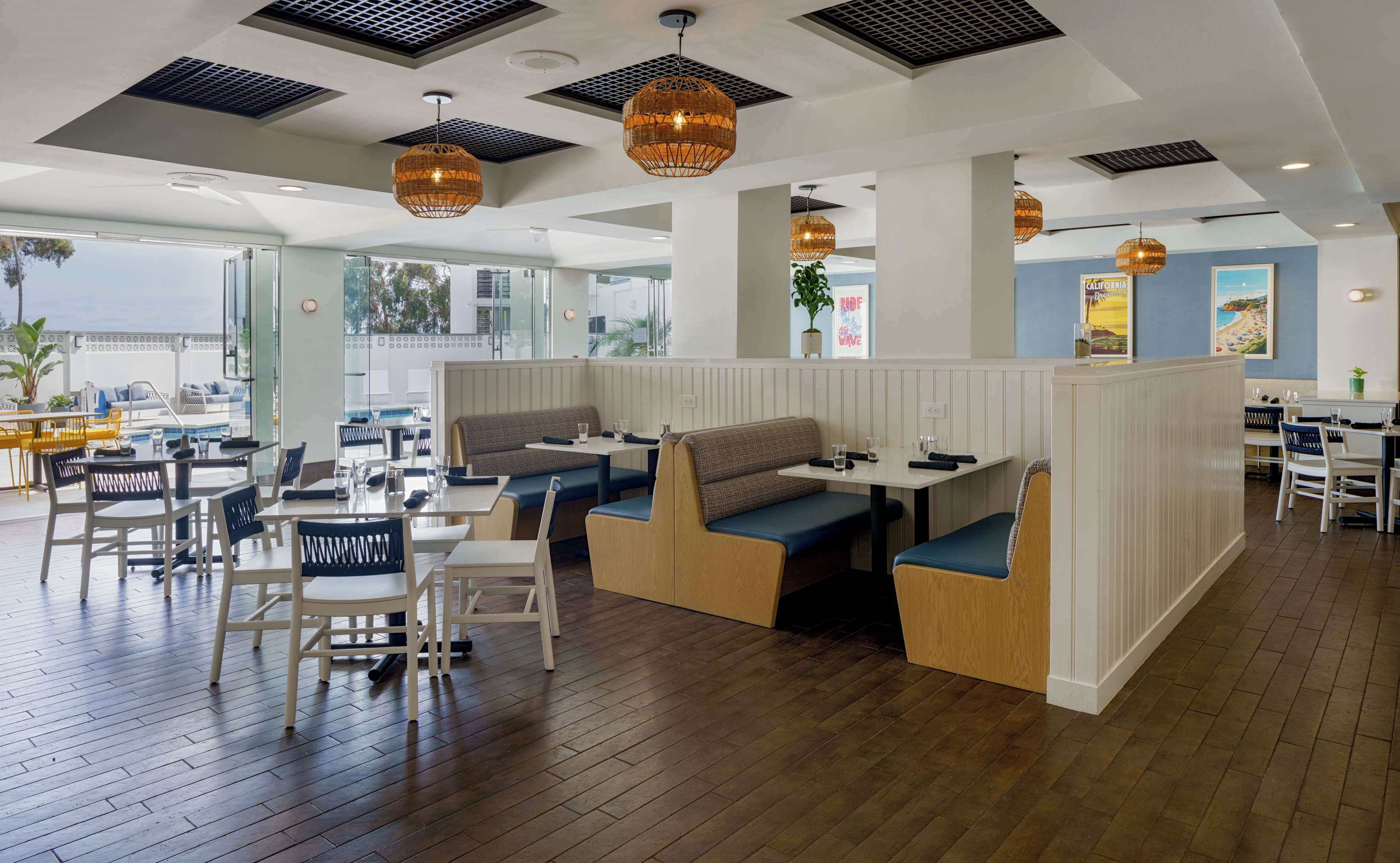 Un interno ristorante moderno con pavimento in legno, sedute bianche e azzurre e lampadari in vimini a sospensione.