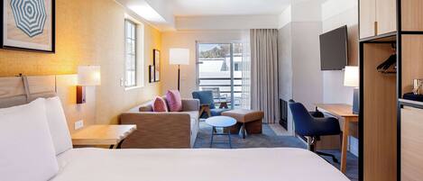Ein Hotelzimmer mit einem großen Bett, einem Schreibtisch, einem Sessel, einer Couch, einem kleinen Tisch und einem Fernseher.