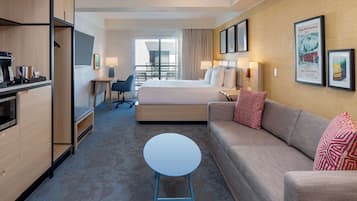 Una habitación de hotel con cama, sofá, una mesita, escritorio, silla y kitchenette.