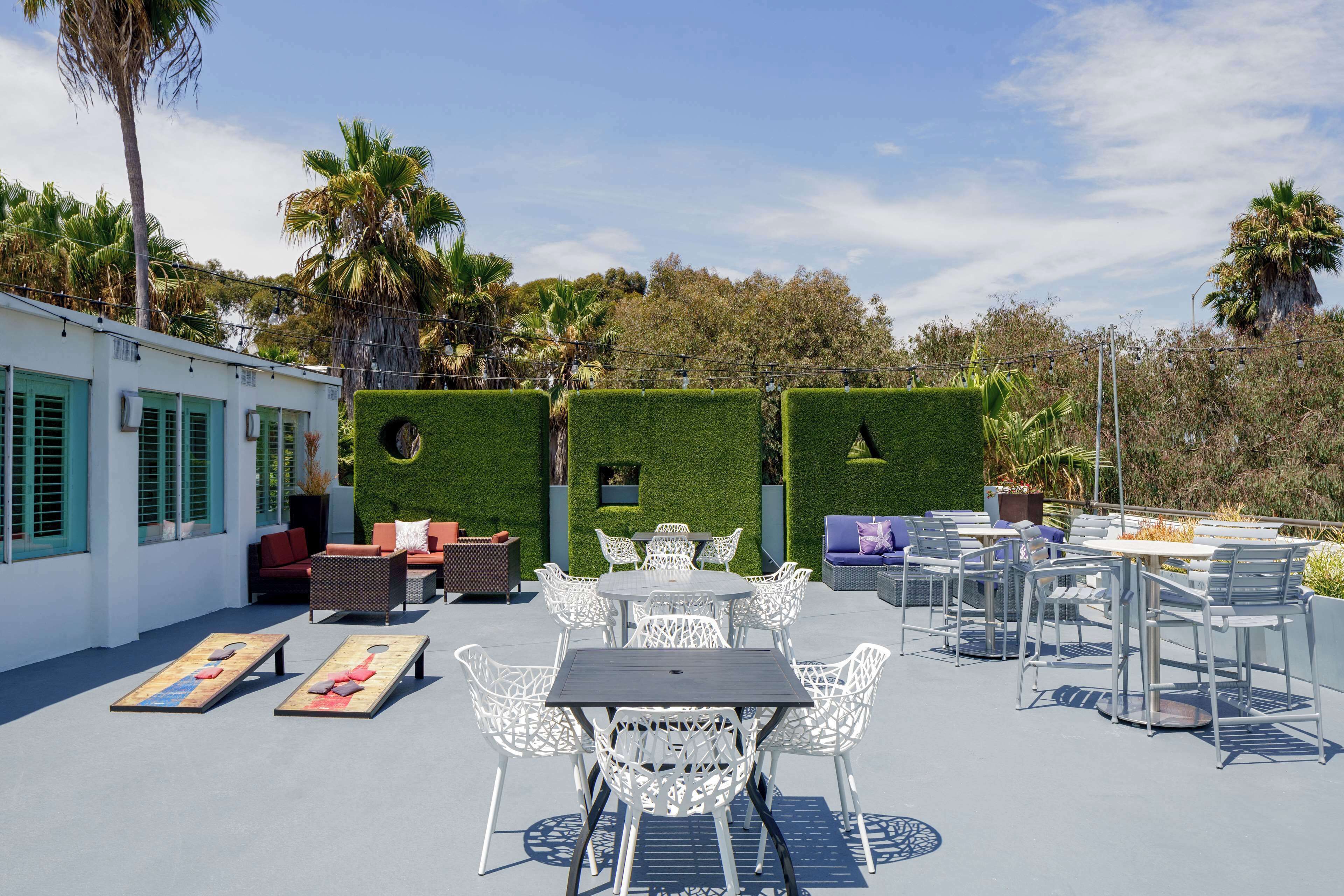 An outdoor patio with white metal furniture, a pool table, and a seating area with a view of palm trees and a building with green shutters.