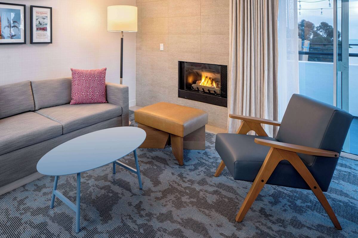 A modern living room with a sofa, a coffee table, a chair, a fireplace, and a view through a window.