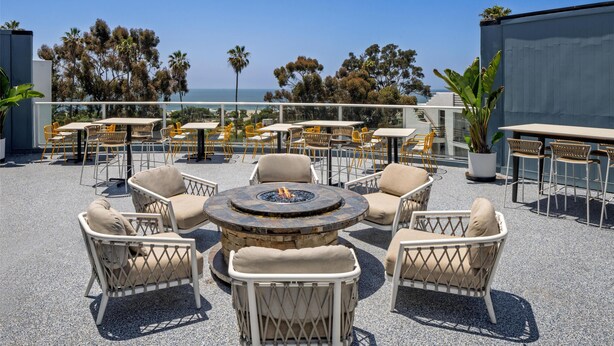 A rooftop patio with outdoor seating, a central fire pit, and a view of the ocean. - Hilton Garden Inn Dana Point Doheny Beach (Dana Point)