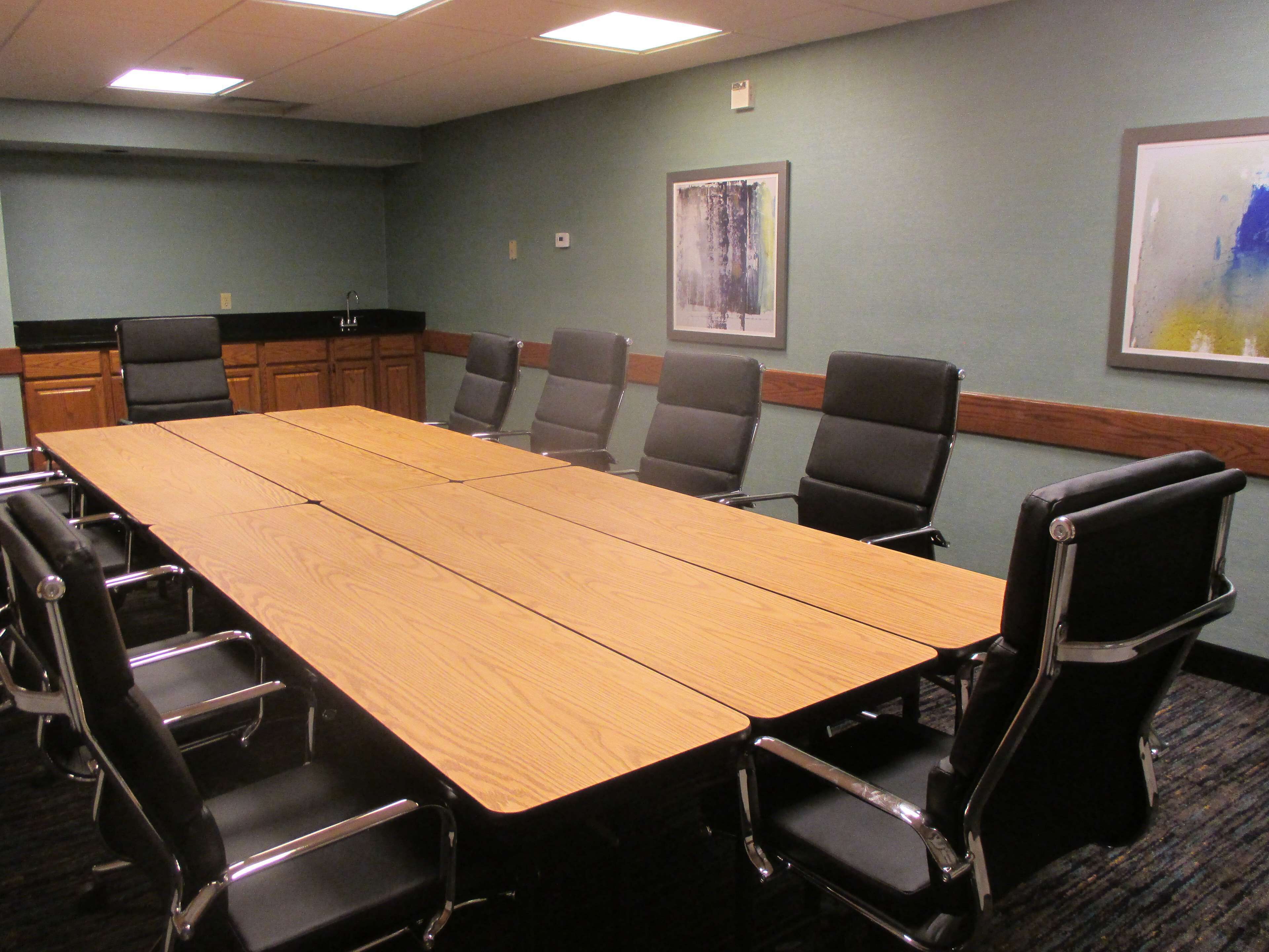 Une salle de conférence avec une longue table en bois, des chaises noires et des œuvres d’art encadrées accrochées aux murs.