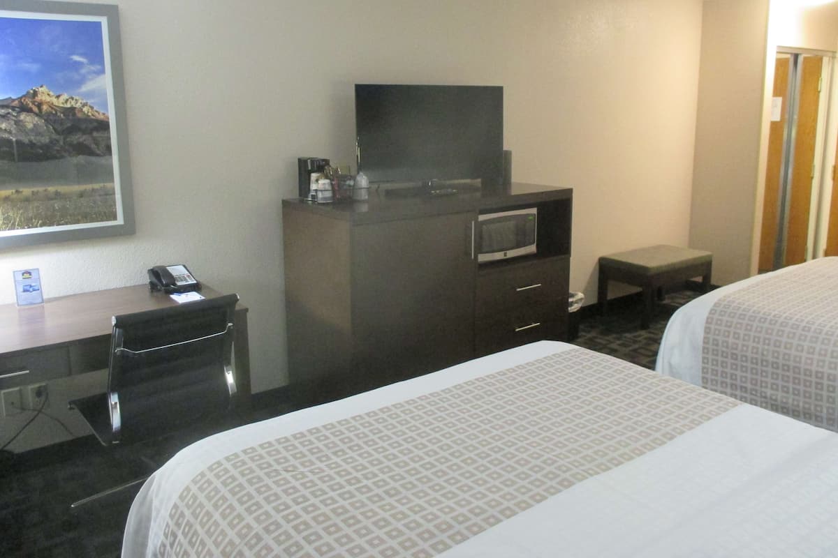 A hotel room with a bed, a desk with a telephone, a television on a dresser, and a small table.